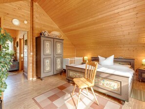 A cozy bedroom with a wooden ceiling, a bed with white linens, a wooden chair, and a dresser with floral designs. - Chalet in Hinterrod Thuringen mit Sauna (Eisfeld)
