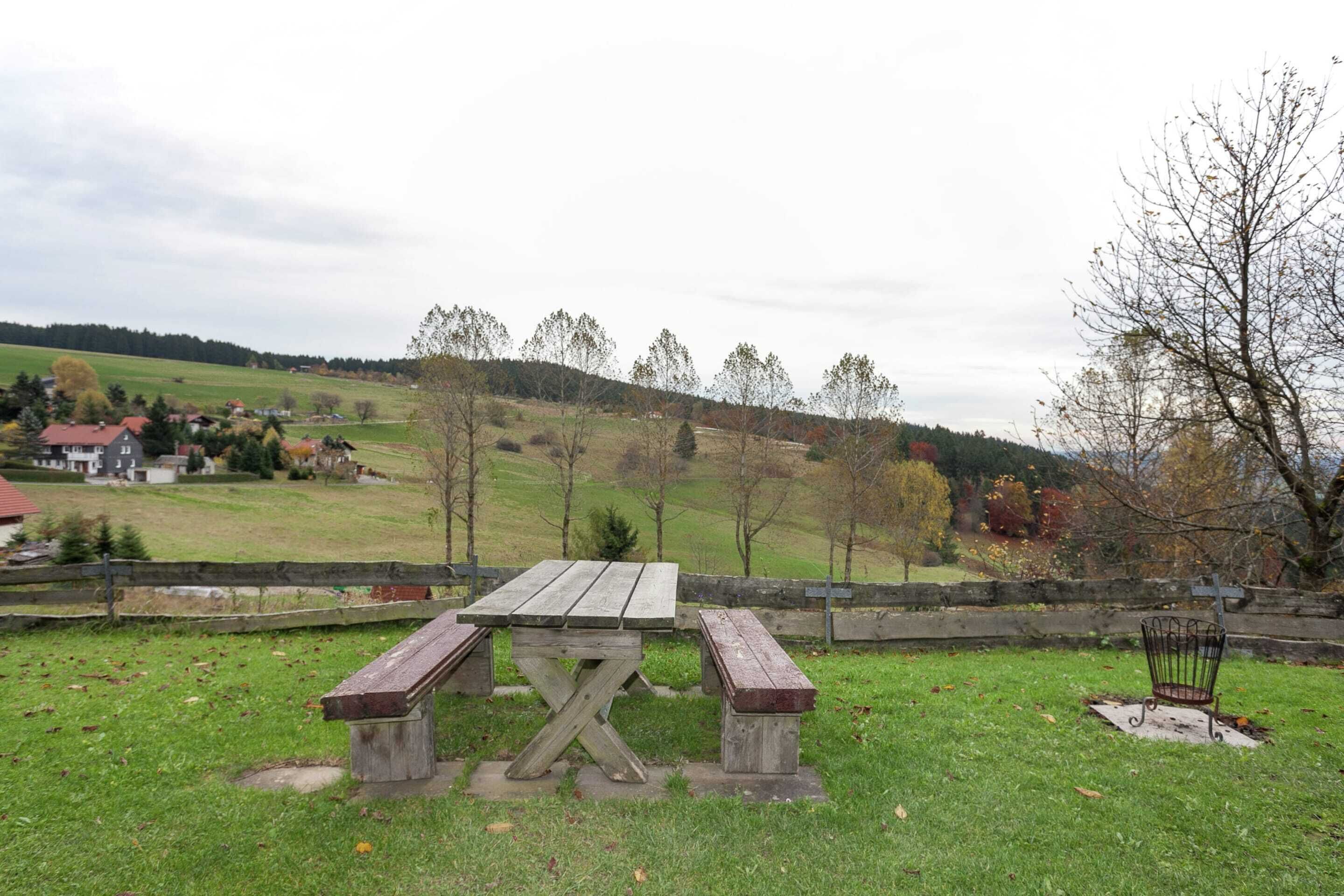 A picnic table with benches in a grassy area with a view of a village and hills in the background.