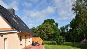 Una casa con patio, un pequeño espacio de estar al aire libre y un jardín cercado.