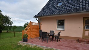 Una casa con techo de tejas, una escalera de madera y un patio con mesa y sillas.