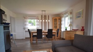 Una sala de estar con sofá, una mesa de comedor con sillas, una zona de cocina con armarios y una ventana con cortinas.