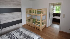 Una habitación con una cama nido, una colcha estampada, suelo de madera y vista a un jardín a través de una puerta.