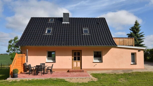 Una casa de dos pisos con techo de tejas oscuras, una puerta principal y dos ventanas.