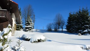 Een besneeuwd landschap met een houten gebouw, besneeuwde bomen en een helderblauwe lucht.
