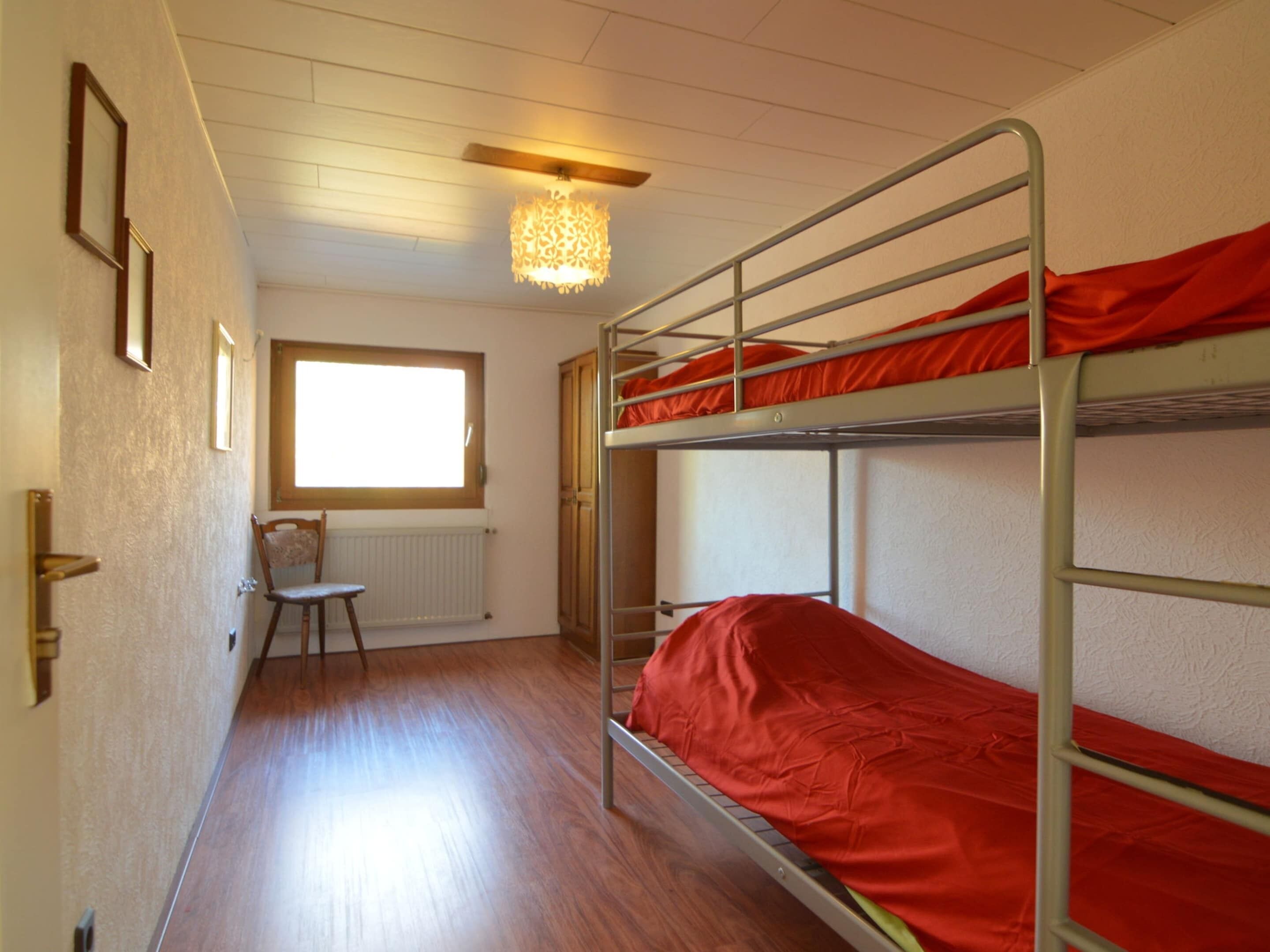 A dormitory room with bunk beds, a radiator, a window, and a chair.