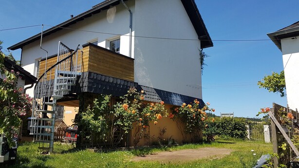 Ein zweigeschossiges Haus mit einer Holzterrasse und einer Metalltreppe.