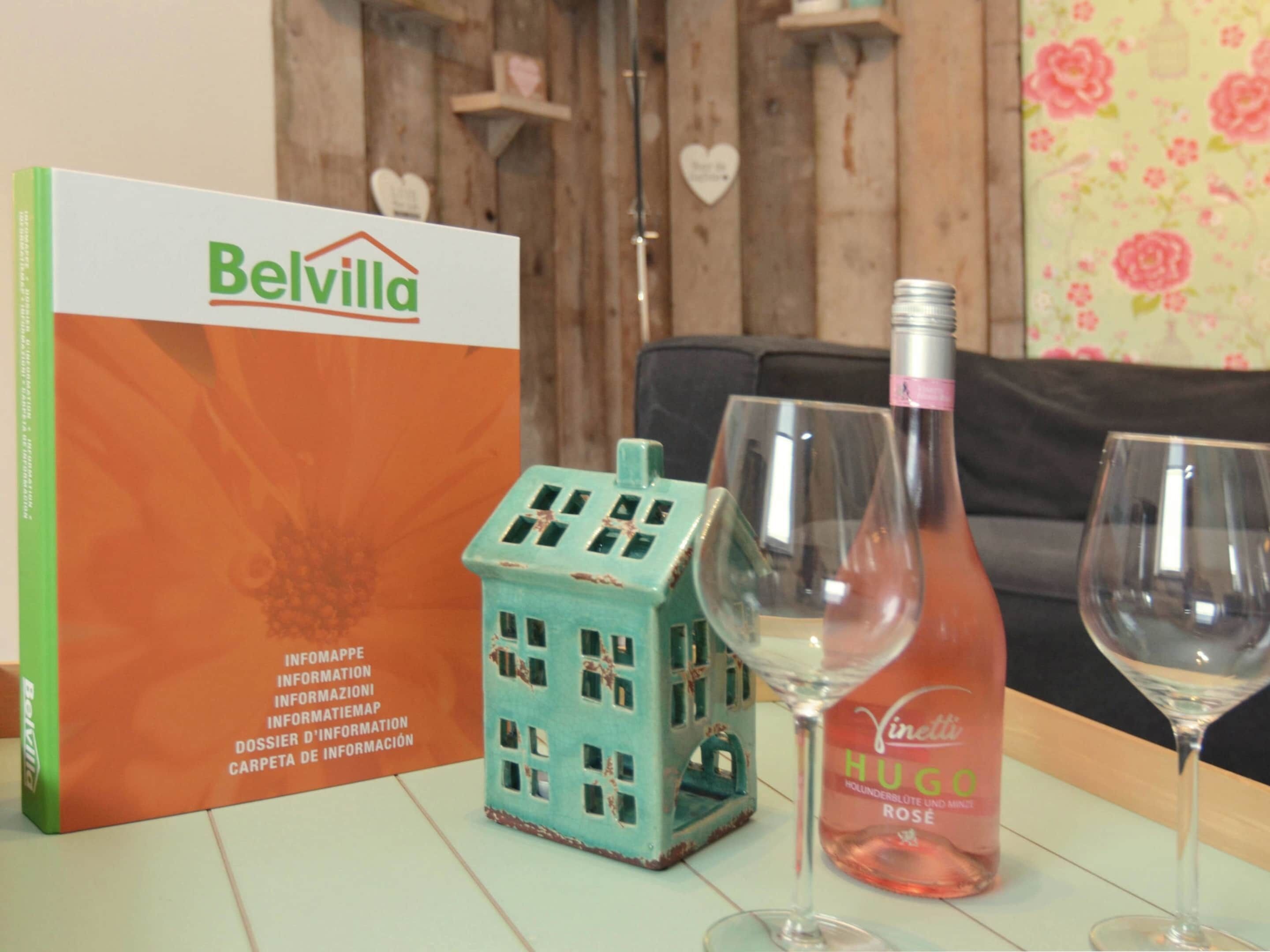A Belvilla box, a small house-shaped object, and two wine glasses on a table.