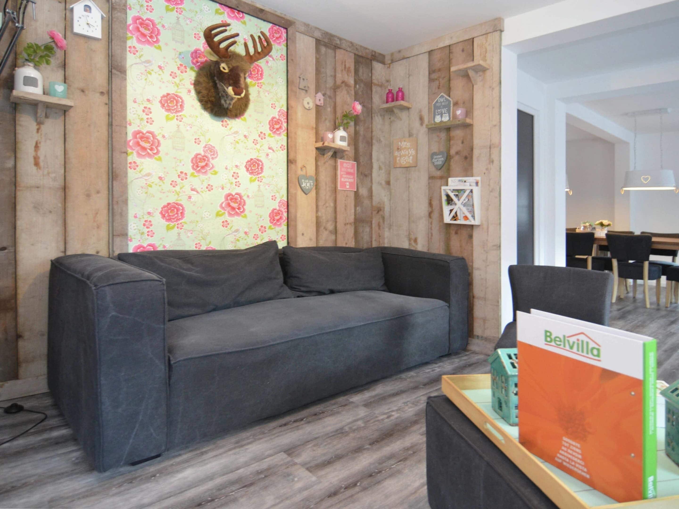 A modern living room with a grey sofa, wooden panel walls, and a floral wallpaper.