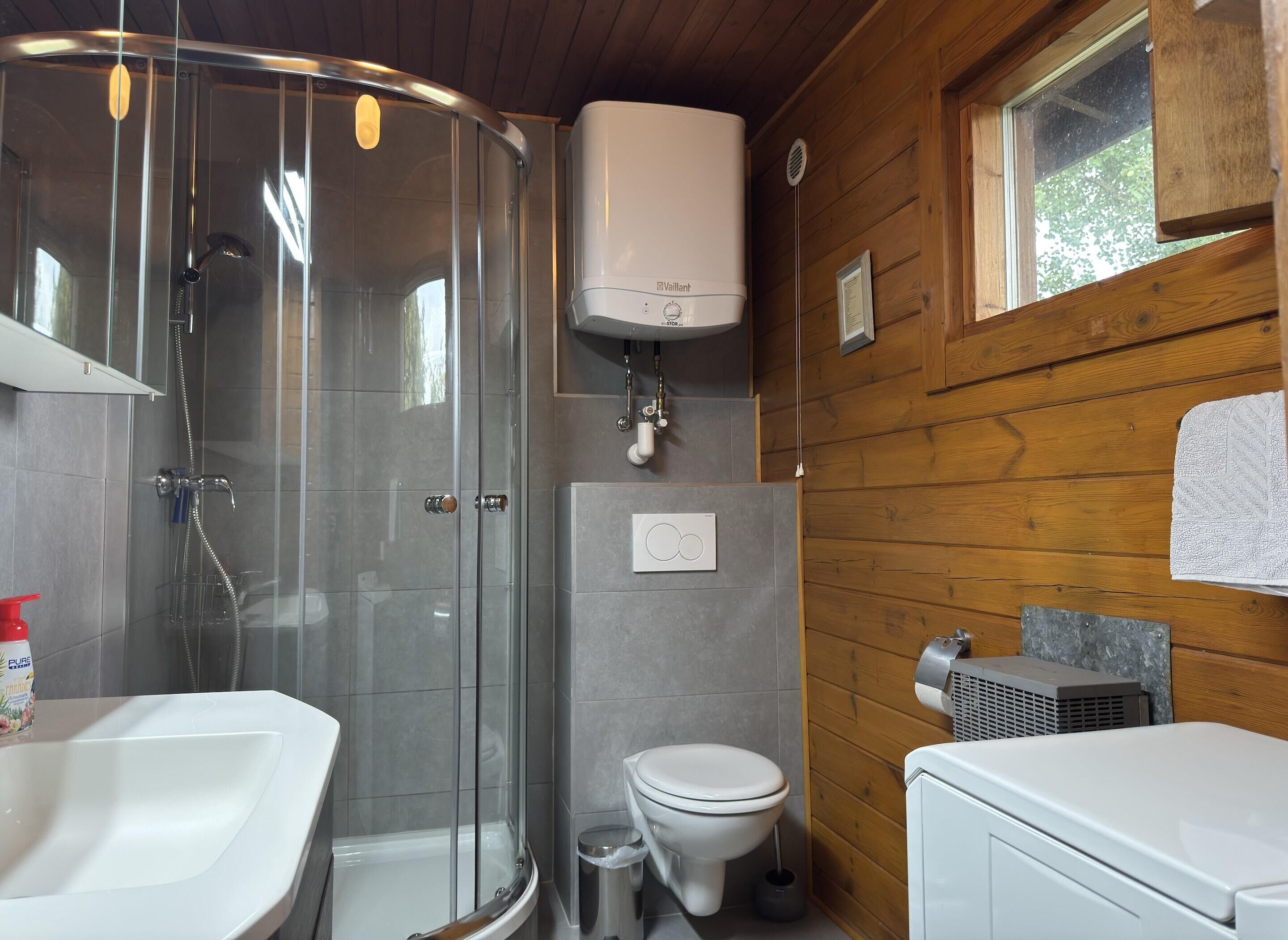 Et moderne badeværelse med et glasafskærmet brusebad, et hvidt toilet og en vask.