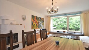 A dining area with a wooden table, chairs, a chandelier, a window with a view of greenery, and a painting on the wall. - Forest-edge Braunlage Home (Braunlage)