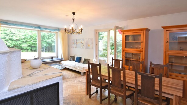 A spacious dining area with a wooden table and chairs, a built-in bookshelf, and a large window offering a view of greenery. - Forest-edge Braunlage Home (Braunlage)