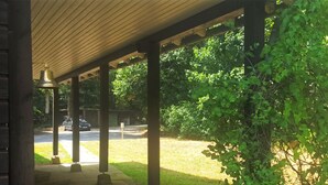 A covered outdoor area with a wooden ceiling and columns, a street view with a parked car, and greenery. - Forest-edge Braunlage Home (Braunlage)