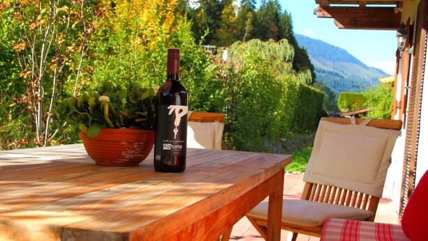 A wooden table with a bottle of Alphome wine, a potted plant, and a chair with a red cushion. - Chalet in Kirchberg With Terrace and Garden (Kirchberg in Tirol)