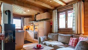 A cozy cabin interior with a wooden ceiling, a kitchen area with cabinets and appliances, a sofa with fur throw, and a table with red candles. - Chalet in Kirchberg With Terrace and Garden (Kirchberg in Tirol)