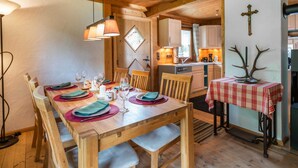 A wooden dining table set with plates, glasses, and cutlery, a kitchen area with cabinets and a sink, and a cross on the wall. - Chalet in Kirchberg With Terrace and Garden (Kirchberg in Tirol)