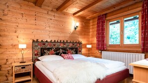 A wooden cabin bedroom with a large bed, two bedside lamps, a red and white patterned headboard, and a window with red curtains. - Chalet in Kirchberg With Terrace and Garden (Kirchberg in Tirol)