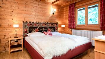 A wooden cabin bedroom with a large bed, two bedside lamps, a red and white patterned headboard, and a window with red curtains.