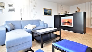 Een moderne woonkamer met een grijze bank, een zwarte entertainmentkast met een televisie en een blauwe fauteuil.