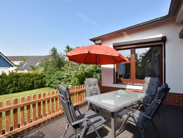 A patio with a glass table and chairs, an umbrella, and a view of a neighboring house.