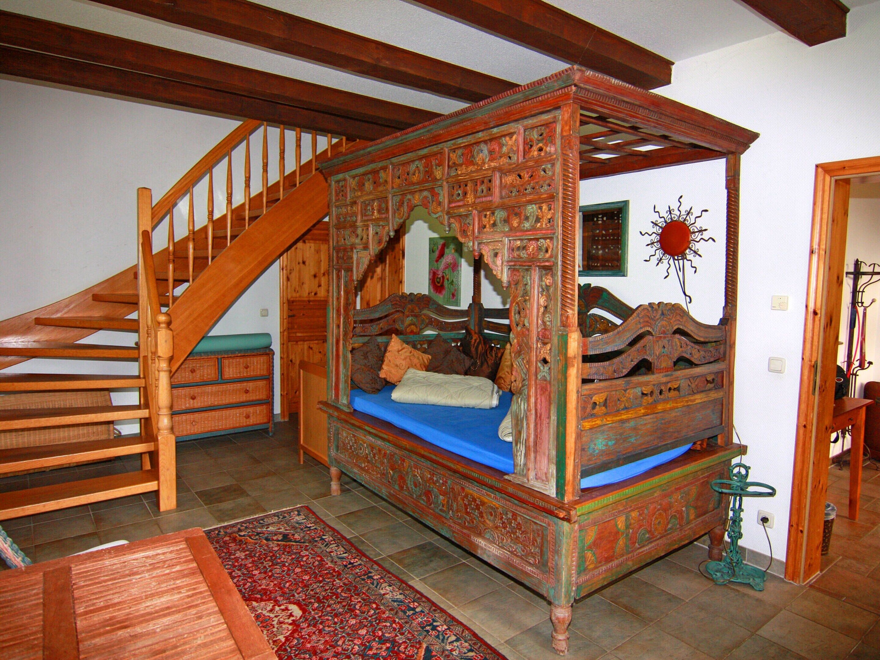 A bedroom with a four-poster bed, a wooden staircase, and a traditional rug.