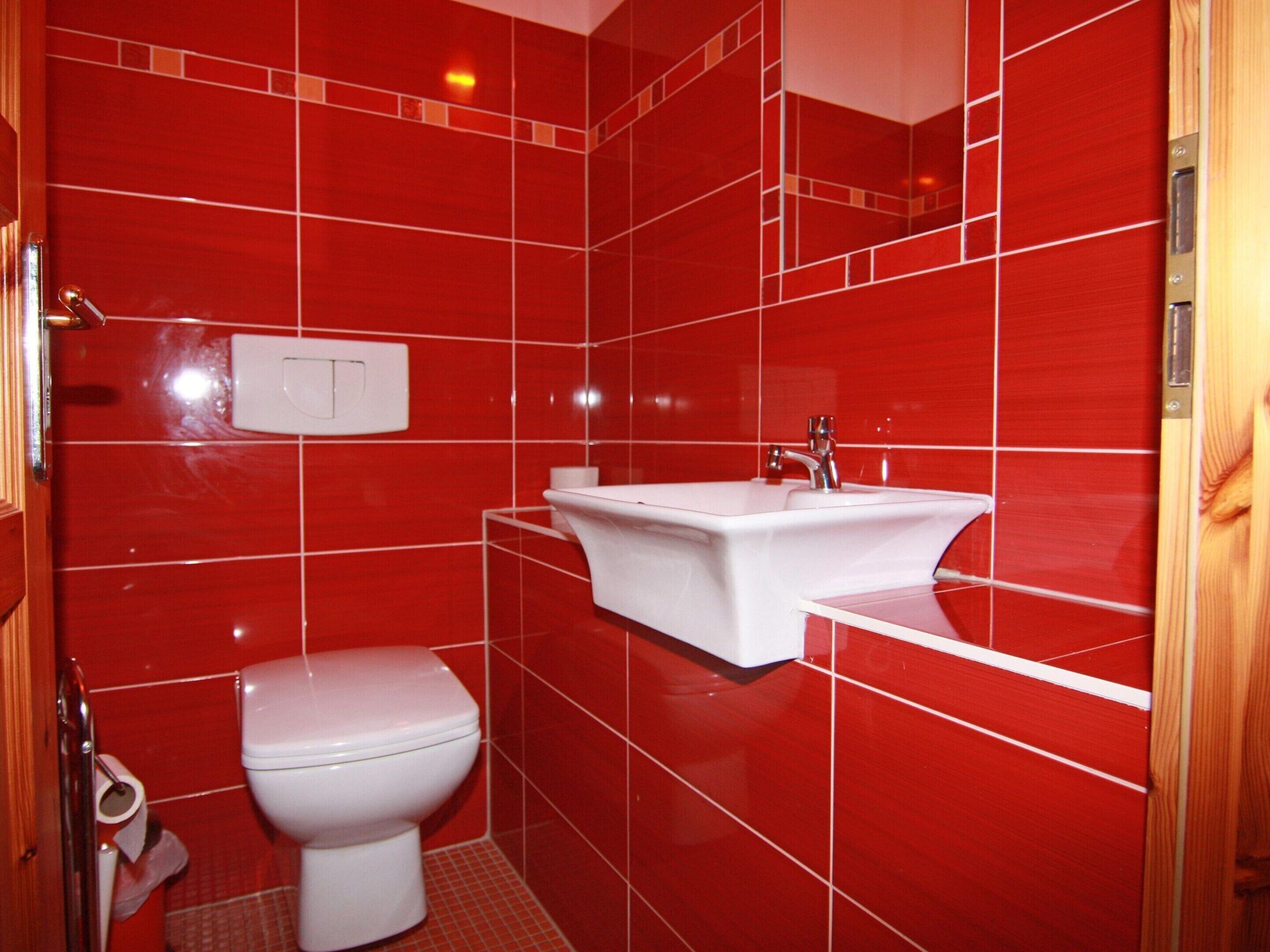 A bathroom with red tiles, a white toilet, and a white sink.