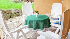 Un espace patio avec une table ronde recouverte d’une nappe verte, entourée de chaises blanches.