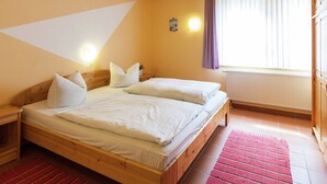 Une chambre avec deux lits, des têtes de lit en bois, un tapis rouge, une fenêtre avec des rideaux et un luminaire fixé au mur.