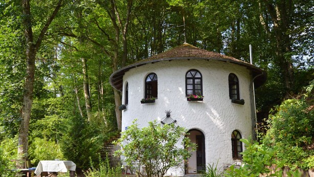 A white, round building with arched windows and a small porch, surrounded by lush greenery and trees. - Strotzbusch Forest Hideaway (Strotzbusch)