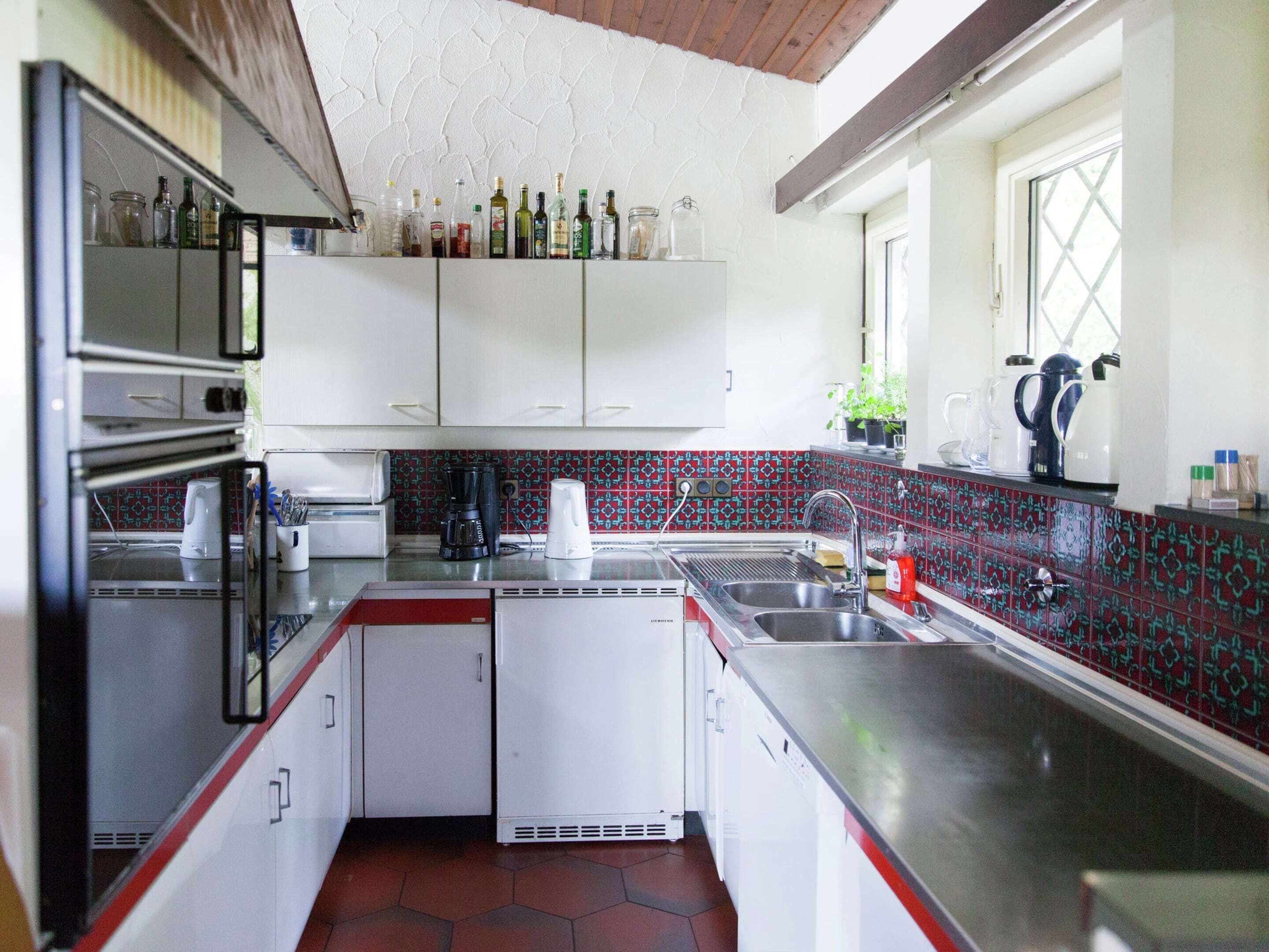 A compact kitchen with white cabinets, a stainless steel countertop, a coffee maker, and a sink.