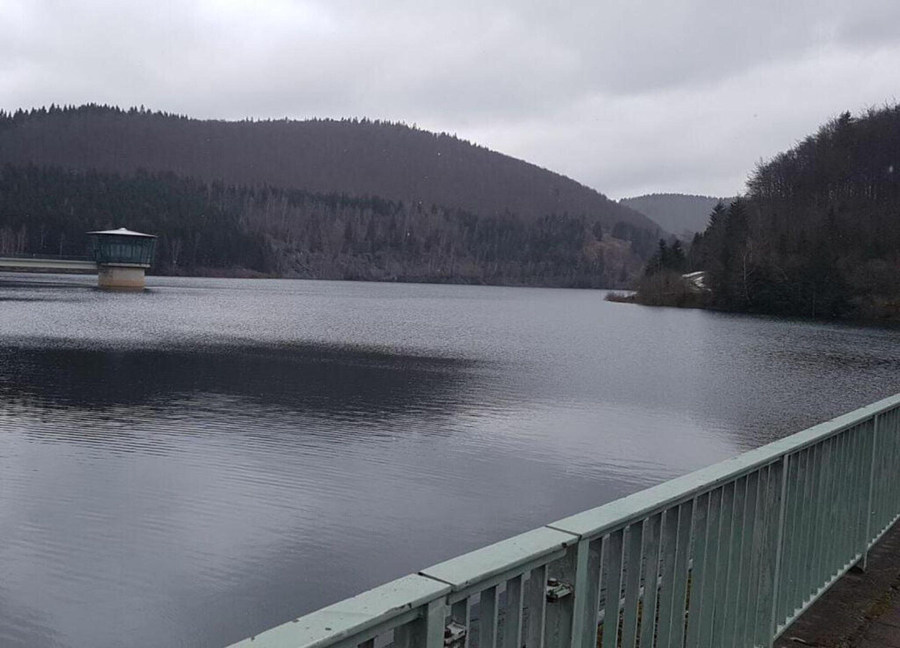 A calm lake with a wooden bridge and a small building on the left.