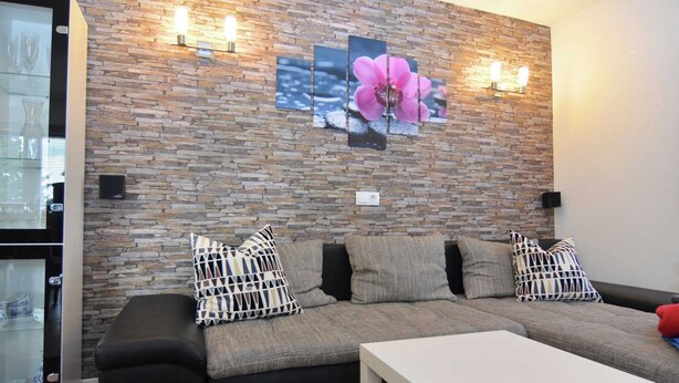 Ein modernes Wohnzimmer mit einer Eckcouch, einem weißen Couchtisch und einer Steinwand mit floralem Kunstwerk.