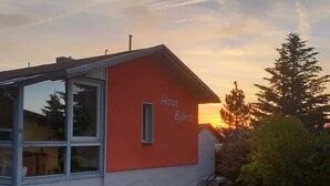 Ein rotes Gebäude mit der Aufschrift "Haus Björn", einem Glasfenster und Blick auf den Sonnenuntergang.