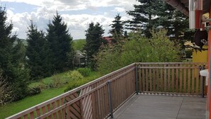 Eine Holzterrasse mit Metallgeländer, umgeben von Grünpflanzen und Bäumen.