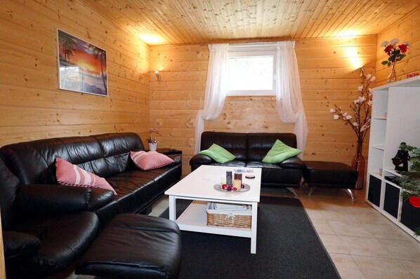 Una habitación acogedora con dos sofás de cuero negro, una mesa de centro blanca y techo de madera.