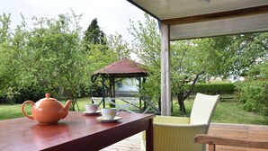 Un terrazzo in legno con un tavolo, un bollitore e due tazze. Si nota una sedia e un gazebo sullo sfondo.