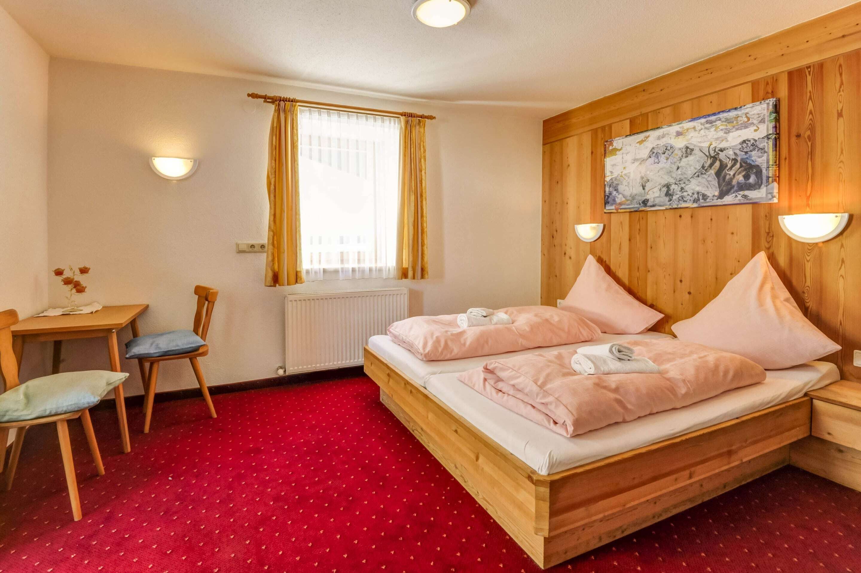 A bedroom with a wooden bed, a desk with a chair, a radiator, and a window with curtains.
