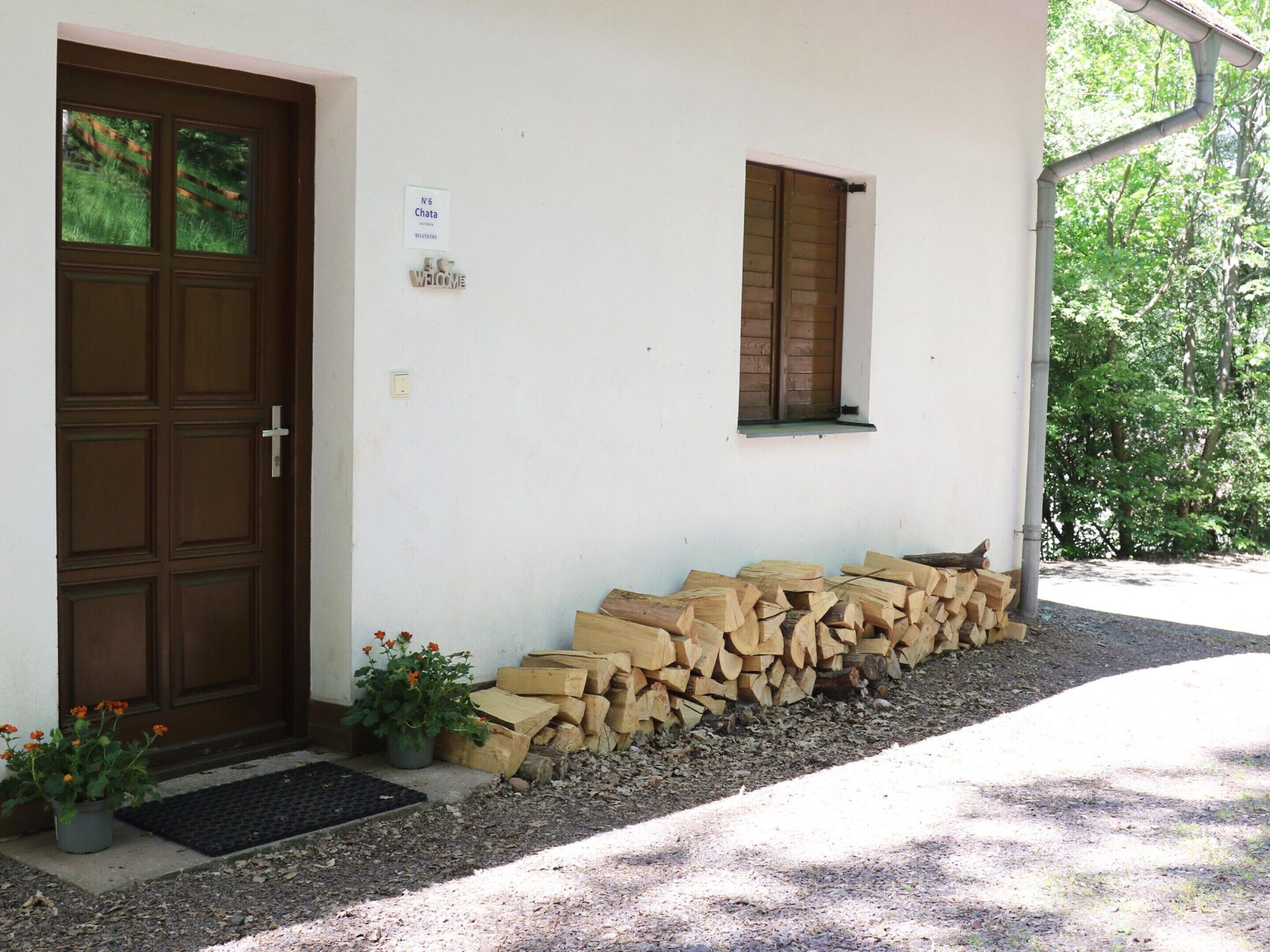 A house with a brown door, a welcome sign, a small window, and a stack of firewood outside.