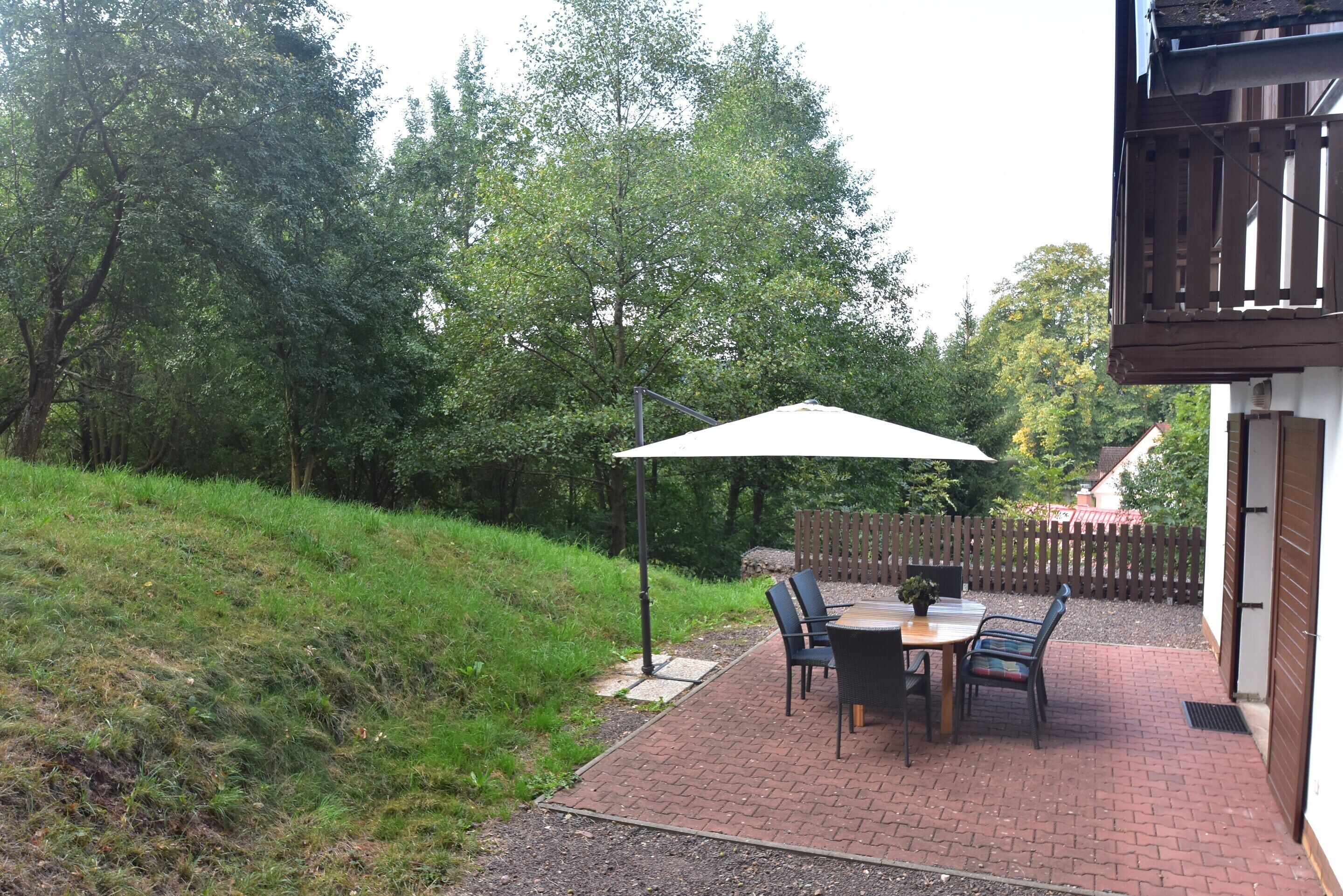 An outdoor patio with a table and chairs, a large umbrella, and a wooden fence in the background.