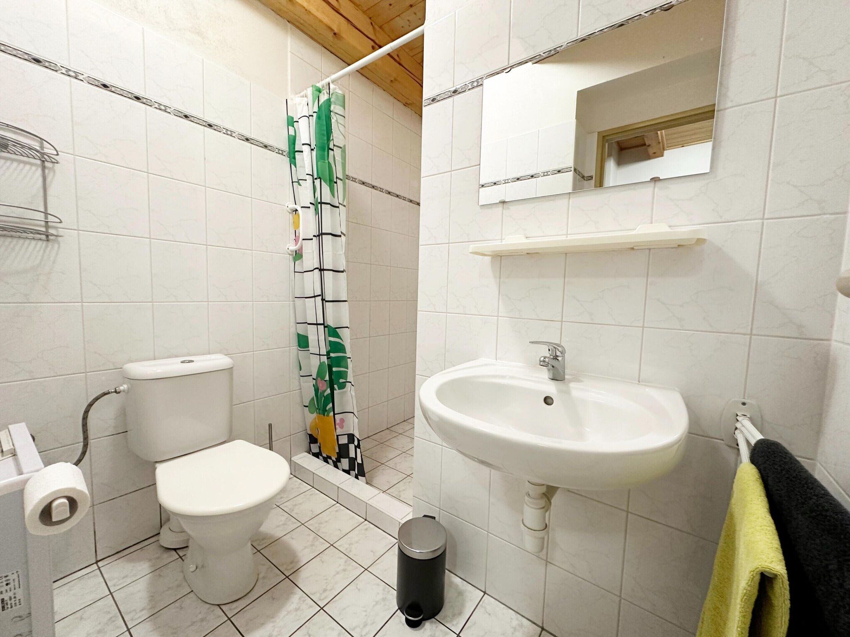 A bathroom with a toilet, a sink, a shower curtain, a trash bin, and a towel rack.