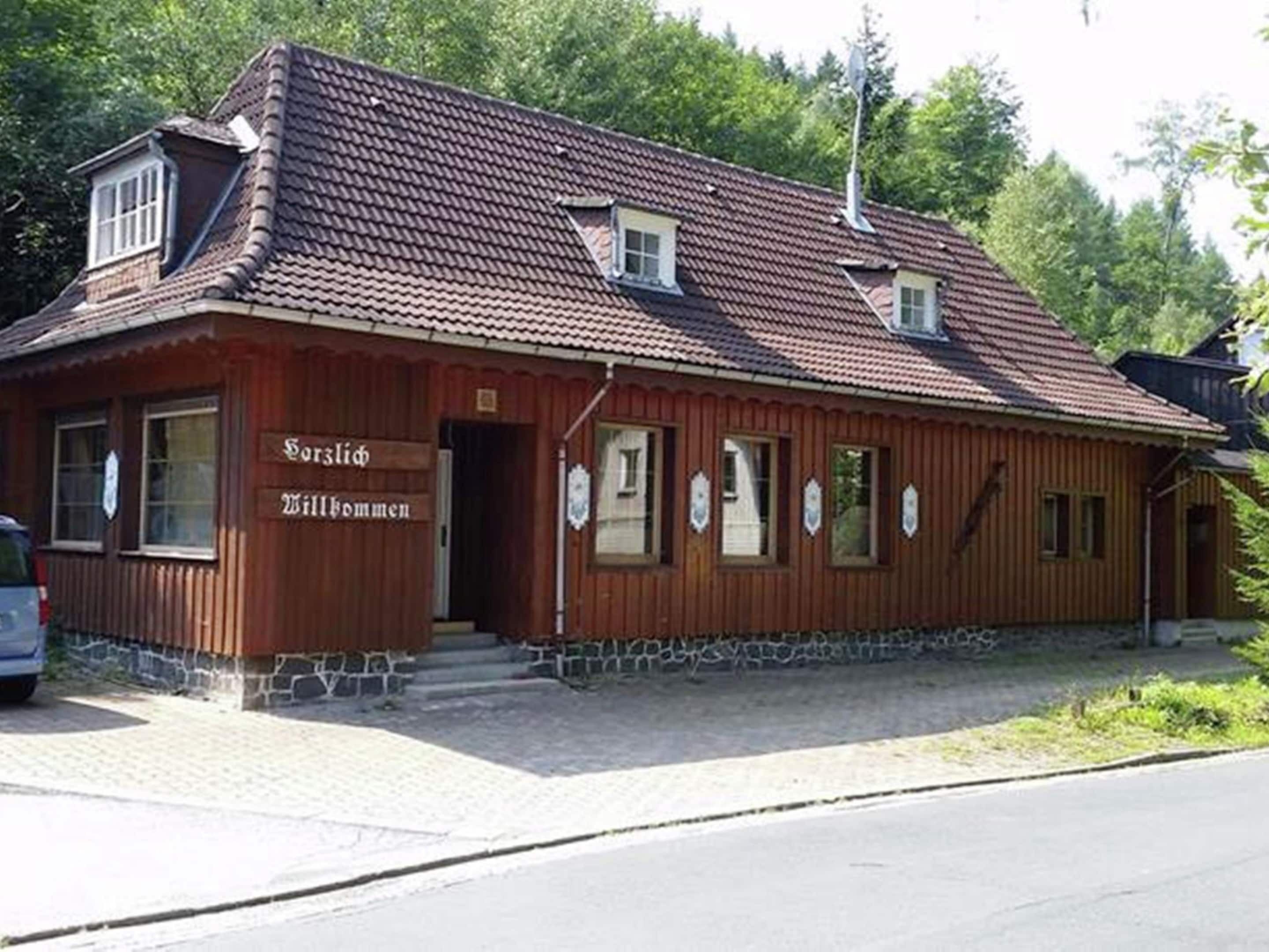 A wooden building with a tiled roof, a sign reading "Sorgepflicht Willkommende", and a small staircase leading to the entrance.