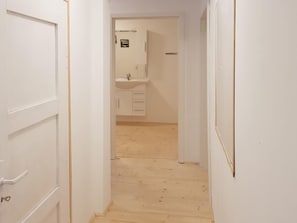 A narrow hallway with white doors and a wooden floor leading to a bathroom with a sink and cabinets. - Ferienwohnung im Oberharz in Wildemann (Clausthal-Zellerfeld)