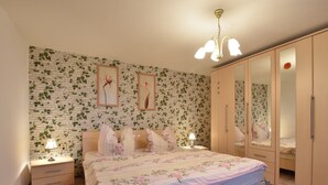 A bedroom with a brick-patterned wall, a bed with floral bedding, bedside lamps, and a wardrobe with a mirror. - Coastal Retreat in Boltenhagen (Boltenhagen)