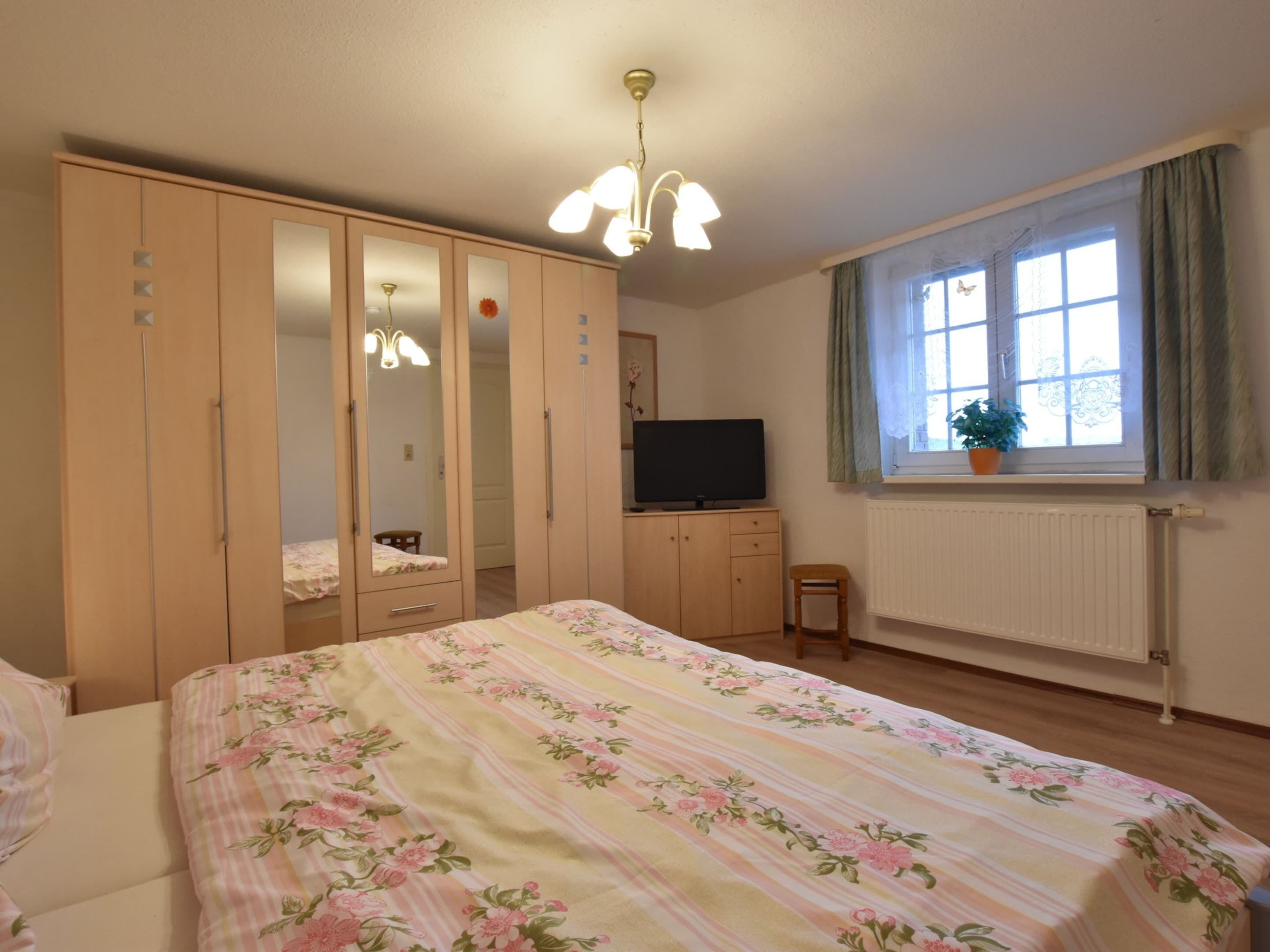 A bedroom with a bed, wardrobe, television, window, and radiator.