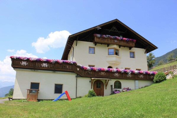 Ein zweistöckiges Gebäude mit einem Balkon, einer Holztreppe und einem kleinen Garten.