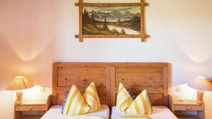 Ein Doppelbett mit gestreifter Bettwäsche, ein Holz-Kopfschild, Nachttische mit Lampen und ein Landschaftsbild an der Wand.