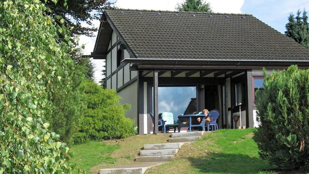 A two-story building with a covered patio area, outdoor seating, and a staircase leading to the entrance. - Holiday Home in Mielinghausen Near ski Area (Meschede)