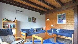 A cozy living room with a wooden ceiling, a blue sofa set, a wooden coffee table, and a bookshelf with books. - Holiday Home in Mielinghausen Near ski Area (Meschede)