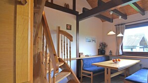 A wooden staircase leading to a dining area with a bench and a table, wooden beams on the ceiling, and a window with a view of a house. - Holiday Home in Mielinghausen Near ski Area (Meschede)