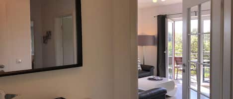 A modern hotel room with a large mirror, a small desk with a basket, and a view of the outdoor balcony area.