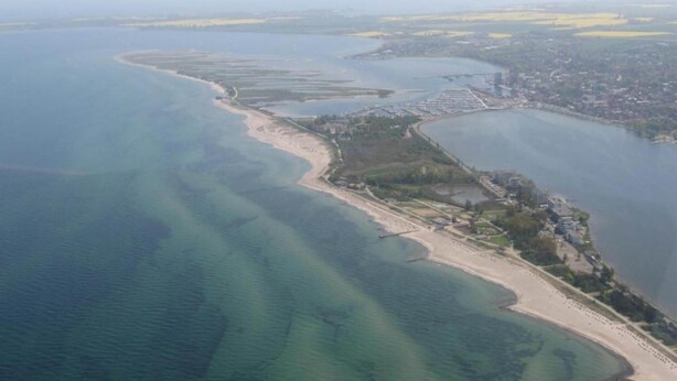 An aerial view of a coastal area with a beach, a marina, and a cityscape in the background. - Familienfreundliches Ferienhaus (Oldenburg in Holstein)